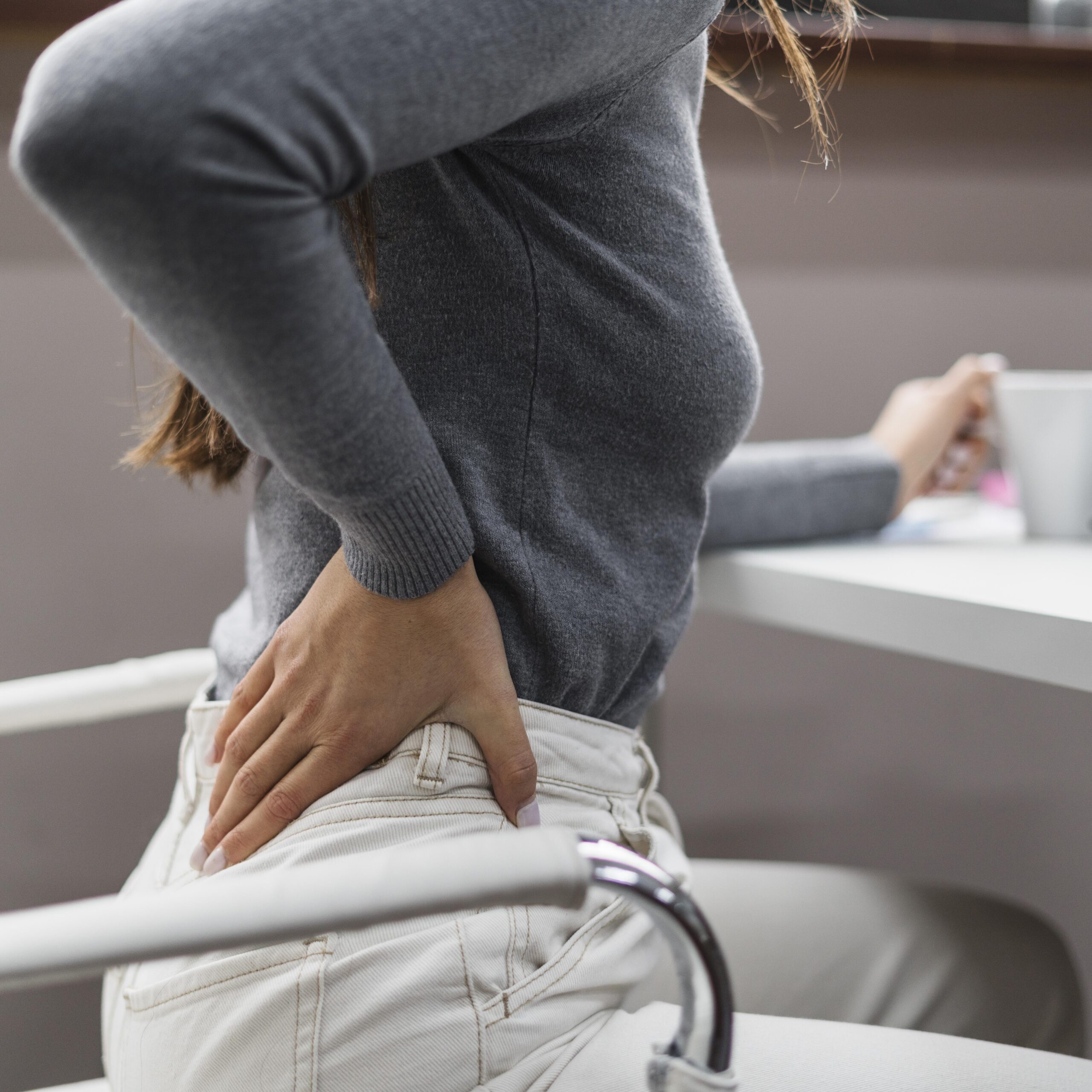 women sitting in office chair with her hand on her back representing like she is in pain