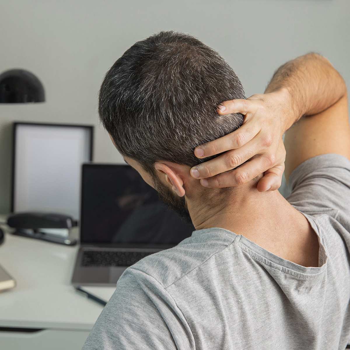 men holding his neck seating at a desk