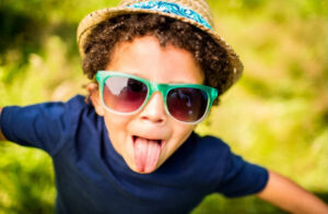 child showing off his tongue with sunglasses and a hat